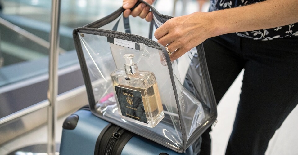A traveler holding a sealed, transparent duty-free bag with a perfume box visible inside, showing the proper way to carry on post-security purchases.