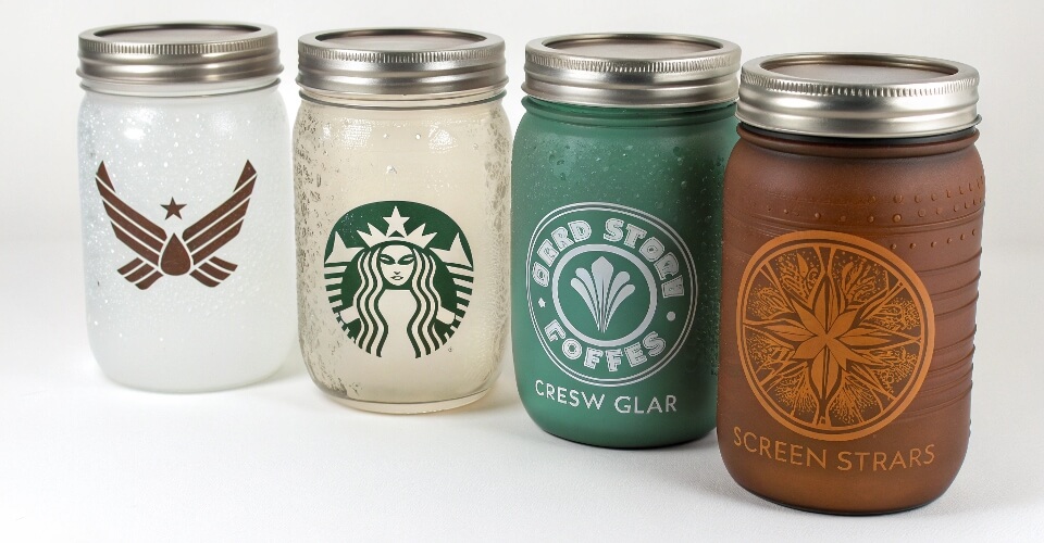 A collection of customized Mason jars showing different surface treatments like frosted glass, colored spray, and screen-printed logos.