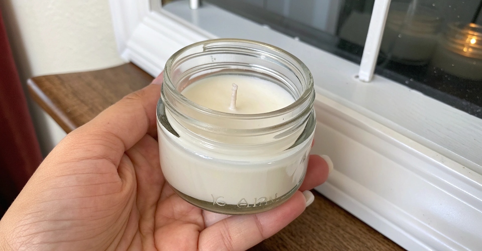 A small, petite 4 ounce clear glass candle jar being held in a person's hand to show its scale.